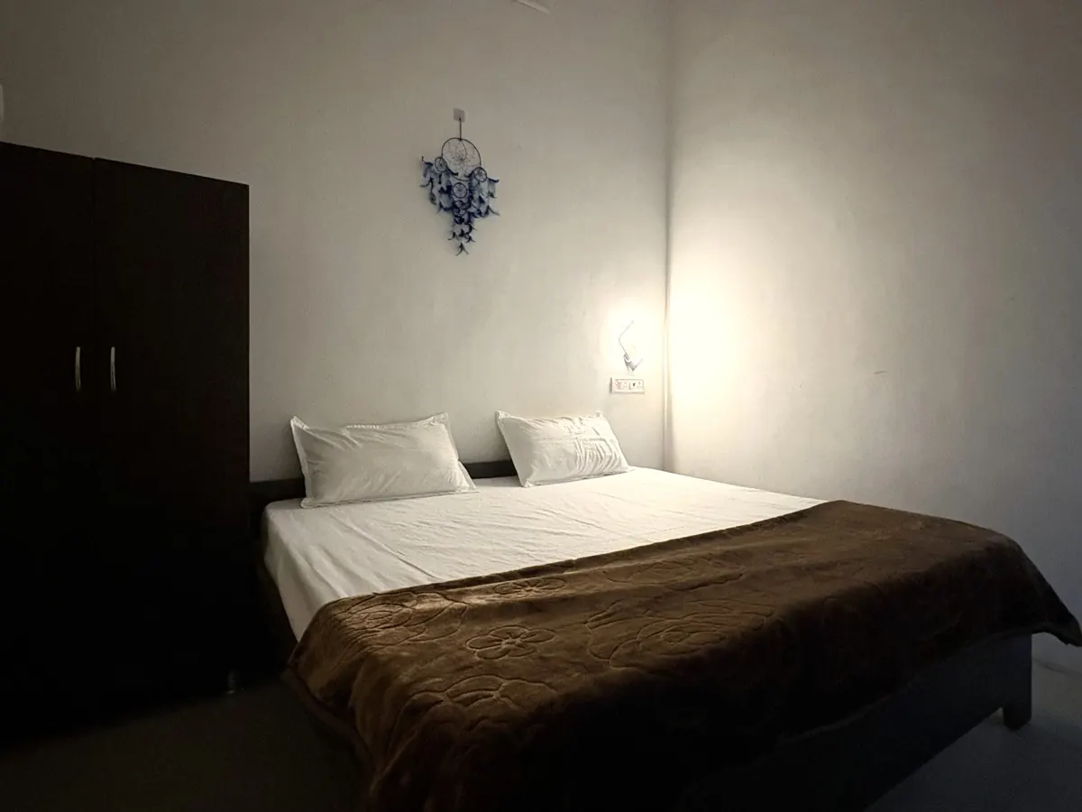 Room 6 at night: bed with a warm brown blanket under a glowing wall lamp